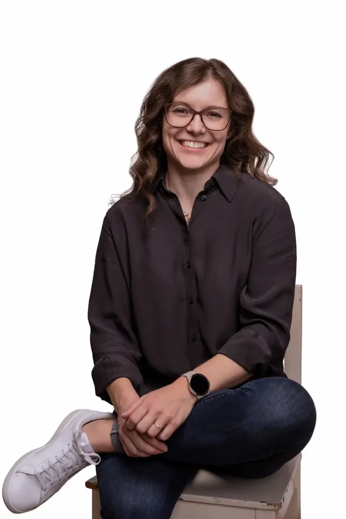 Eva Brucksch, Expertin für Positive Leadership, sitzt entspannt auf einem Stuhl und blickt lächelnd in die Kamera.